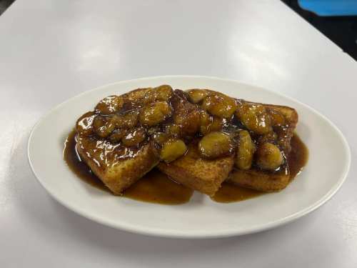 A plate of French toast topped with caramelized bananas and a rich syrup.