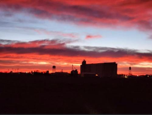 Silhouetted buildings against a vibrant sunset with red and orange clouds illuminating the sky.