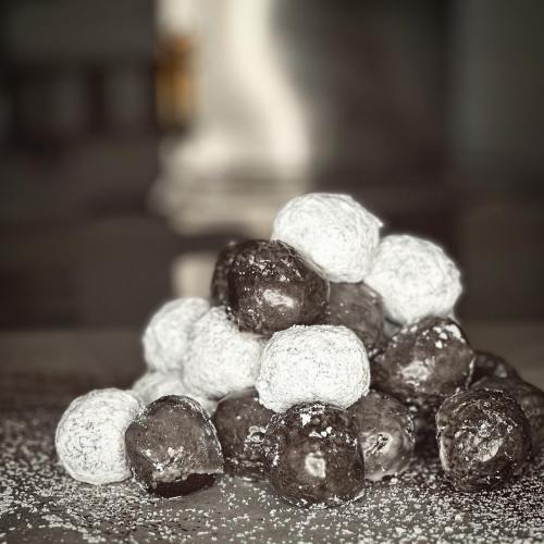 A pile of chocolate and powdered sugar-coated dessert balls on a textured surface.
