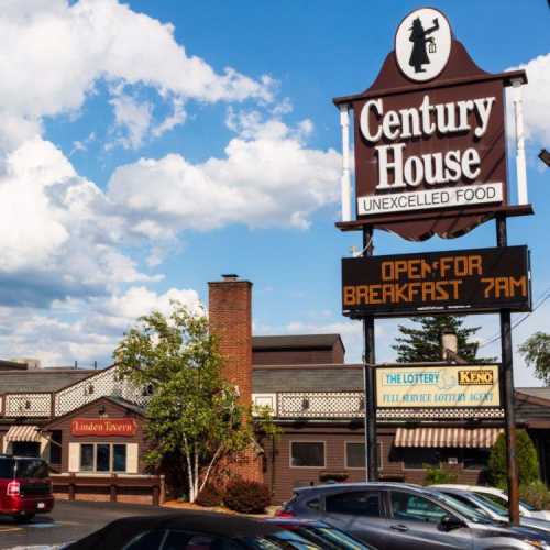 Sign for Century House with "Open for Breakfast 7 AM" displayed, alongside a building and blue sky with clouds.