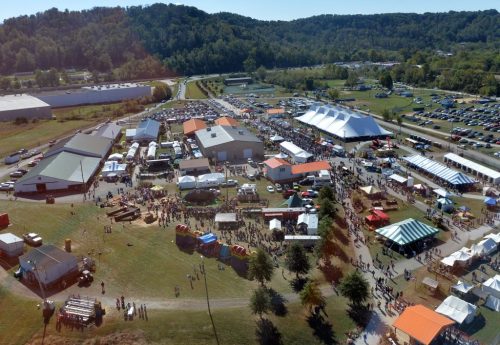 Aerial view of a bustling outdoor festival with tents, food trucks, and crowds in a scenic landscape.