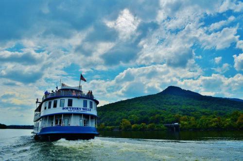 A riverboat named "Southern Belle" sails on a calm waterway, with lush green hills and a cloudy sky in the background.