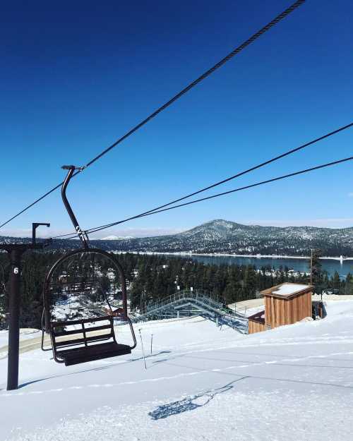 A ski lift chair against a snowy landscape, overlooking a lake and mountains under a clear blue sky.