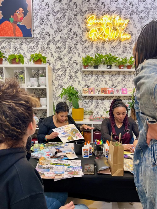 A group of people engaged in a creative activity at a table, surrounded by plants and colorful art supplies.