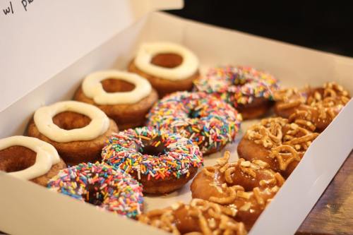 A box of assorted donuts, including frosted, sprinkled, and pretzel-topped varieties.