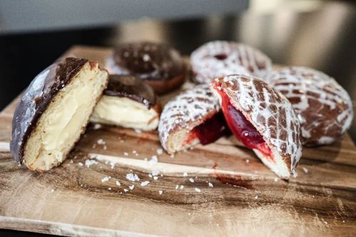 A wooden board with assorted donuts: one filled with cream, others with fruit filling, some topped with chocolate and icing.