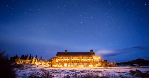 A cozy lodge illuminated at night, surrounded by snow and a starry sky.