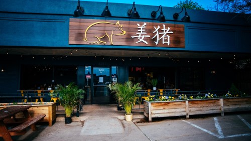 Exterior of a restaurant featuring a pig logo, outdoor seating, and decorative plants. Brightly lit with string lights.