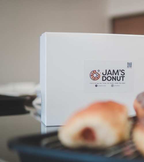 A white box labeled "Jam's Donut" with a donut in the foreground, resting on a black tray.