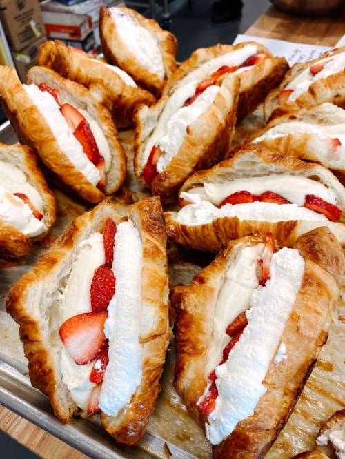 A tray of flaky croissants filled with whipped cream and fresh strawberries, arranged neatly.