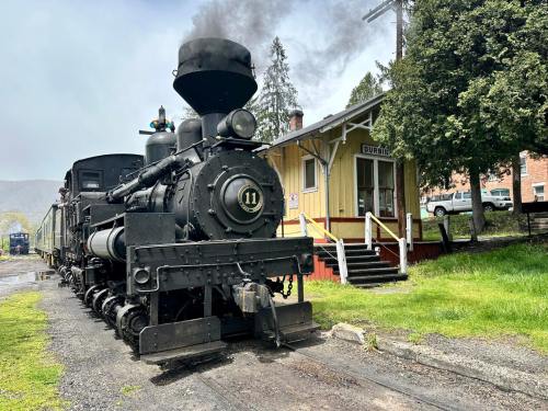 A vintage steam locomotive parked near a yellow train station, with smoke billowing from its chimney.