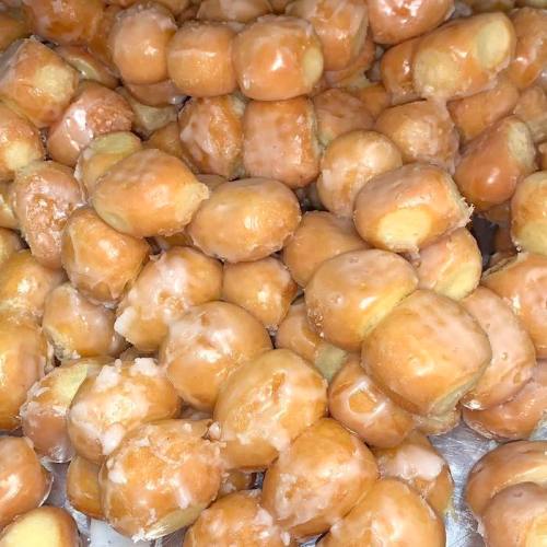 A close-up of glazed doughnut holes piled together, showcasing their shiny, sugary coating.