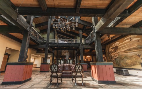 Interior of a spacious lodge with wooden beams, a chandelier, and a cozy seating area featuring two chairs.