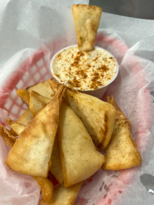 A basket of crispy tortilla chips with a small cup of creamy dip sprinkled with seasoning.