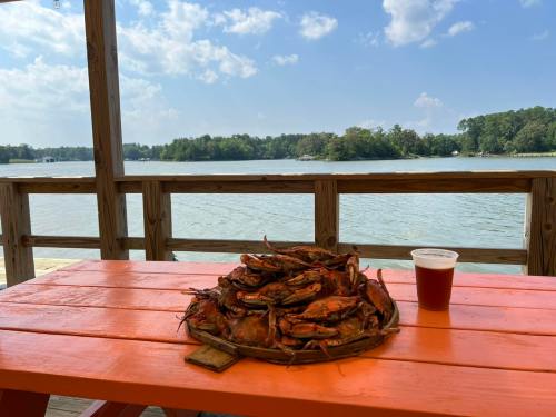 A platter of crabs on an orange table by a lake, with a drink beside it and a scenic view of trees and clouds.