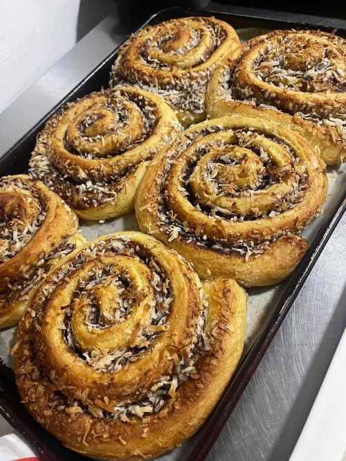 A tray of freshly baked cinnamon rolls topped with shredded coconut, golden brown and spiraled.