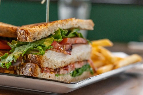 A close-up of a sandwich with lettuce, tomato, and turkey, served with a side of golden French fries.