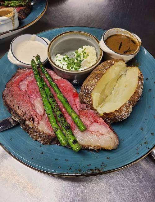 A plate with prime rib, asparagus, a baked potato, and sauces, including sour cream and gravy, on a blue dish.