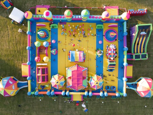Aerial view of a colorful inflatable bounce house with various slides and play areas, filled with children playing.