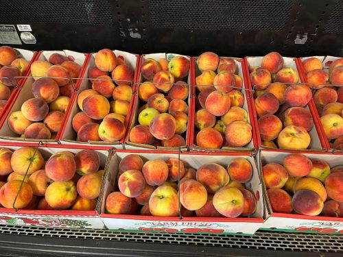 A display of fresh peaches in cardboard boxes at a grocery store.