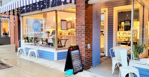 A cozy café with outdoor seating, large windows, and a chalkboard menu outside, illuminated by string lights.