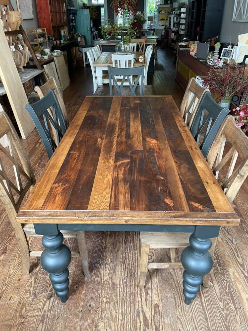 A wooden dining table with a striped top and dark legs, surrounded by chairs in a cozy, rustic interior.