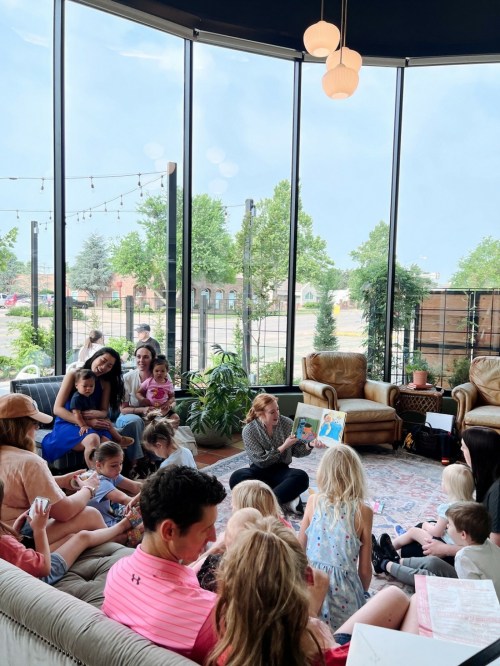A group of children and adults gather in a cozy space for a storytime session, with a storyteller reading a book.