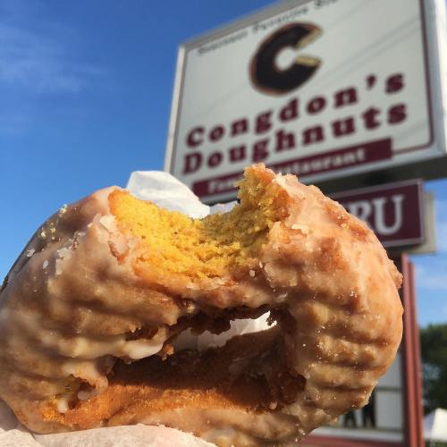A partially eaten glazed doughnut in front of a sign for Congdon's Doughnuts.