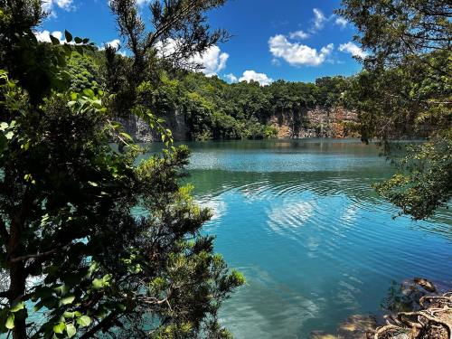 A serene lake surrounded by lush greenery and rocky cliffs under a bright blue sky with fluffy clouds.