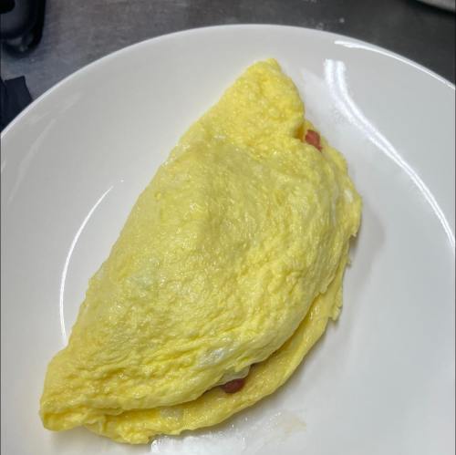 A fluffy yellow omelette on a white plate, filled with diced tomatoes.