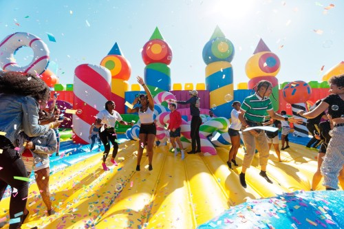 A vibrant bounce house party with people dancing and confetti in the air, surrounded by colorful inflatable decorations.