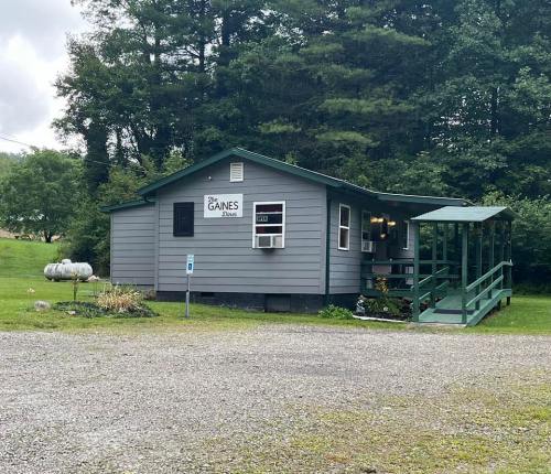A gray house with a green porch and sign reading "Gaines" surrounded by trees and gravel parking.