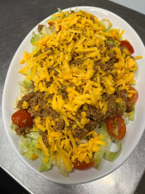 A large salad topped with shredded cheese, ground beef, cherry tomatoes, and a bed of lettuce on a white platter.