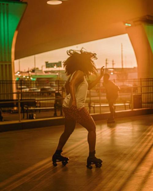 A person roller skating indoors at sunset, with warm light illuminating the scene and a second skater in the background.