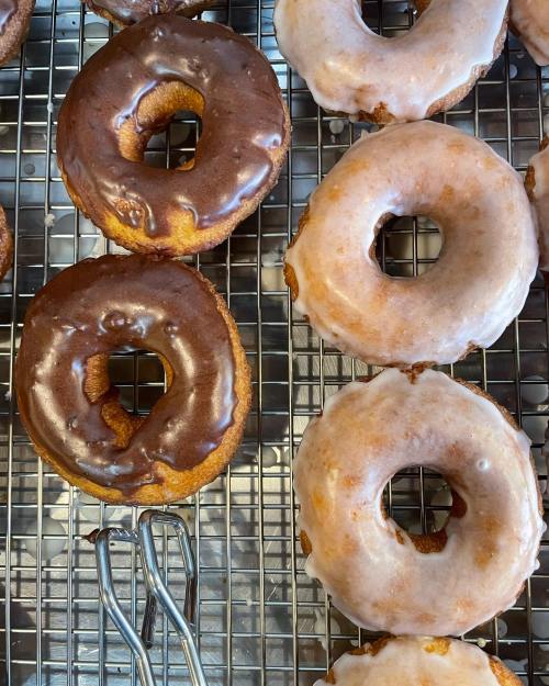 A tray of freshly baked donuts, featuring chocolate-glazed and plain glazed varieties on a cooling rack.