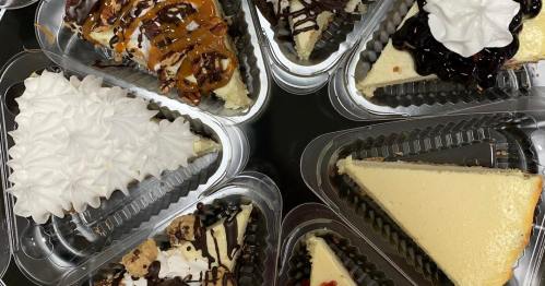 A variety of cheesecake slices topped with whipped cream, chocolate, caramel, and fruit, arranged in clear containers.