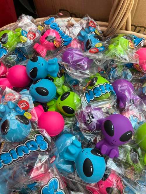 A basket filled with colorful alien-shaped toys in various shades of blue, pink, green, and purple, all in packaging.