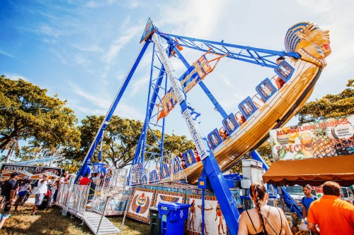 A colorful amusement park ride with a Pharaoh theme, surrounded by trees and people enjoying the fair.