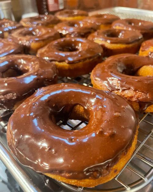 A close-up of freshly glazed chocolate donuts cooling on a wire rack.