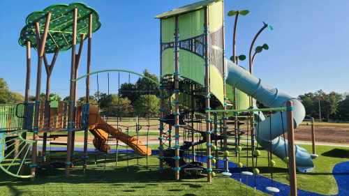 Colorful playground with a slide, climbing structures, and green trees under a clear blue sky.