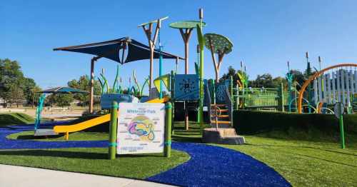 Colorful playground with slides, climbing structures, and shaded areas, surrounded by green grass and blue pathways.