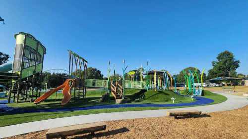 A colorful playground with slides, climbing structures, and green landscaping under a clear blue sky.