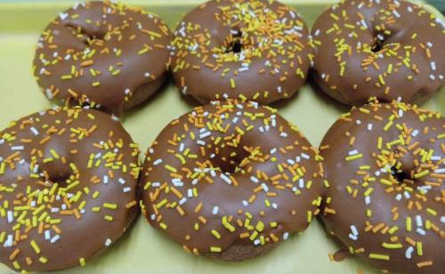 A tray of six chocolate-covered donuts topped with yellow and white sprinkles.