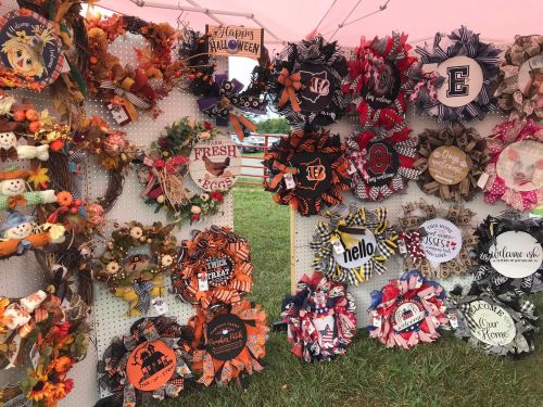 A display of colorful seasonal wreaths, featuring Halloween and autumn themes, hanging on a white pegboard.