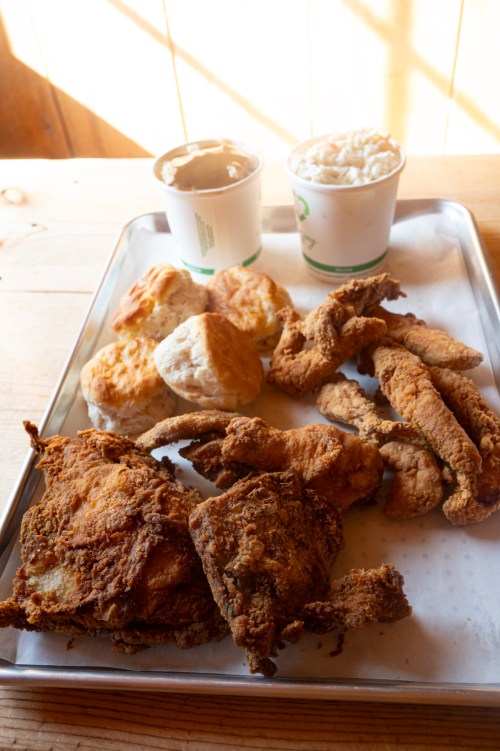 A tray of fried chicken, biscuits, and two cups of creamy sides on a wooden table.