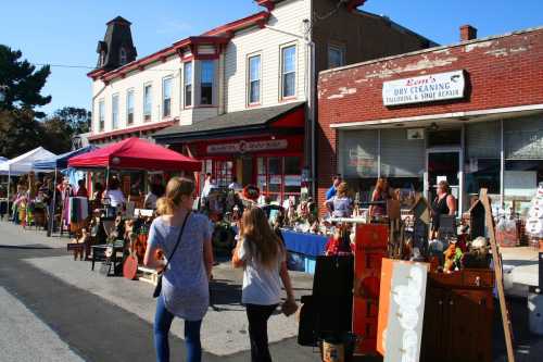 A bustling street market with vendors, colorful tents, and people browsing various handmade goods and decorations.