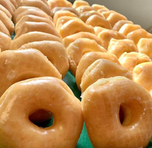 A close-up view of freshly glazed donuts arranged in a row on a green surface.