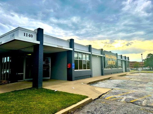 A gray commercial building with large windows, featuring a sign that reads "Halloween Express" and a cloudy sky above.