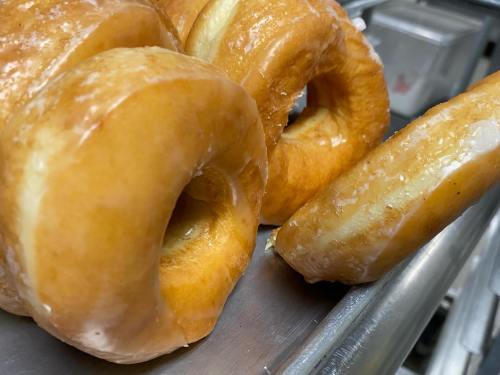 Close-up of glazed donuts on a metal tray, showcasing their shiny, golden-brown surfaces.