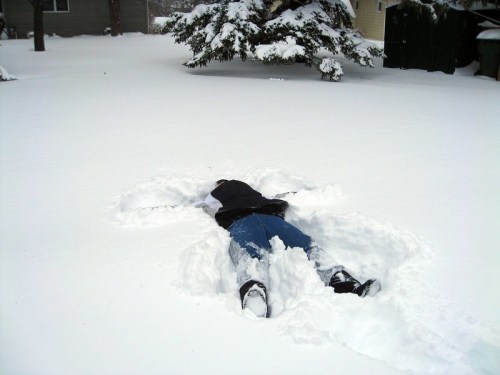 A person lying face down in deep snow, creating a snow angel shape in a winter landscape.